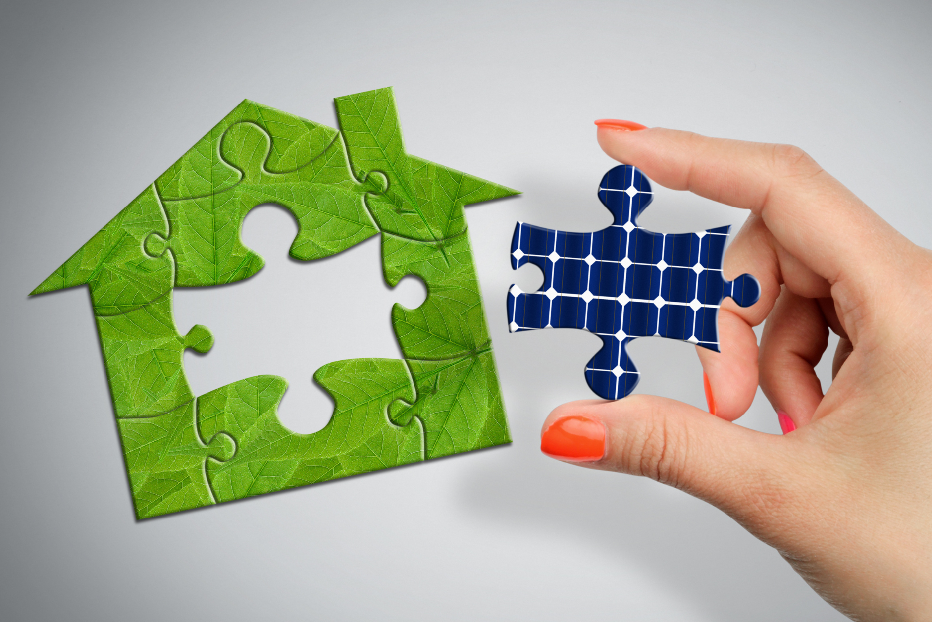 une main de femme ajoute une pièce de puzzle représentant un panneau photovoltaïque sur une maison